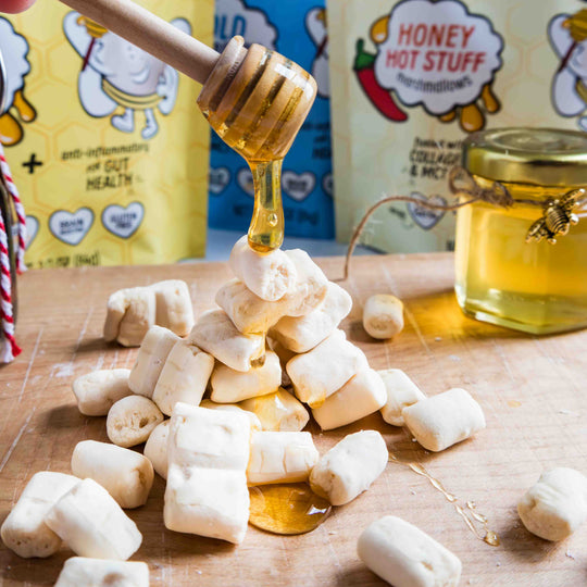 Honey being drizzled over marshmallows with Max Mallo and Honey Now products in the background.